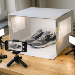 Osoba fotografuje telefonem buty w domowym lightboxie DIY na białym tle z lampkami LED